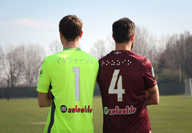 Foto di due giocatori di spalle della AC Reggiana, indossano la maglia con i propri nomi scritti in Braille